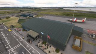A green-roofed airport terminal displays Scottish and British flags, with a red-and-white twin-engine aircraft parked on the apron beside coastal runways.