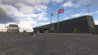 Scottish and Union flags fly outside a low airport terminal, with a silver van and several people near the entrance.