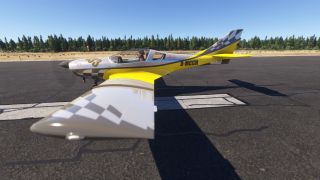 A yellow and silver propeller aircraft with checkered wings and tail sits on a runway, with a pilot visible in the cockpit.