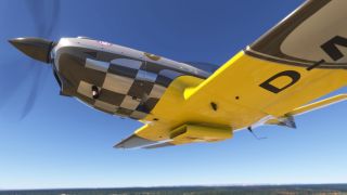 A propeller aircraft flies overhead, showing a yellow underside, black-and-white checkered cowling, and blurred propeller against a clear blue sky.
