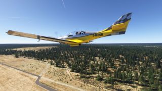 A yellow and black single-engine aircraft flies low above forest and dry clearings, with a winding paved road below.