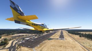 A yellow single-engine aircraft flies above runway 21, with parked airplanes, airport buildings, and surrounding forest visible below.