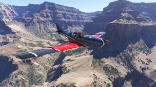 A black and red single-engine aircraft with two visible occupants flies through a rocky canyon dotted with sparse green vegetation.