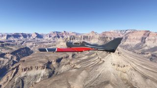 A black and red light aircraft flies above layered canyon cliffs, with a winding river below and clear blue sky overhead.