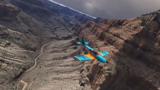 A turquoise and orange light aircraft flies through a rocky canyon above a winding stream beneath dark clouds.