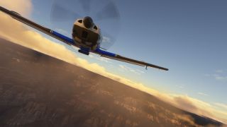 A blue single-engine aircraft flies above rugged terrain, viewed from below its nose with a blurred propeller and golden clouds behind.