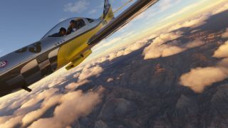 A yellow and silver jet with two visible occupants banks above rugged canyons and scattered clouds lit by low sunlight.