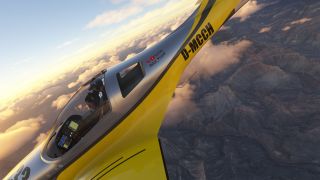 A yellow and silver aircraft banks steeply above rugged canyons and scattered clouds, with two headset-wearing occupants visible beneath its canopy.