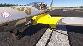 A yellow and gray light aircraft sits on runway markings with two headset-wearing occupants beneath its bubble canopy.