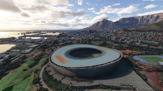 An oval stadium with DHL roof markings dominates the foreground, with a harbor, dense city buildings, and flat-topped mountains beyond.