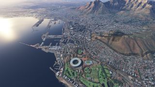 An aerial view shows a coastal city with harbor basins, an oval stadium, green parkland, and steep mountains behind dense neighborhoods.
