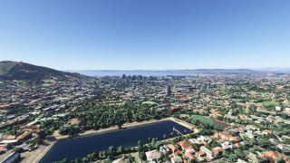 A rectangular reservoir sits among tree-lined neighborhoods, with downtown high-rises, a coastal harbor, and a green hillside beyond.