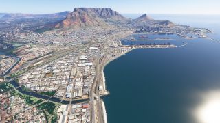 Cape Town spreads beneath Table Mountain, with harbor basins, dockside cranes, industrial buildings, and coastal roads visible from above.