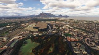 A coastal city spreads around large commercial buildings and waterways, with a flat-topped mountain rising beneath scattered clouds.