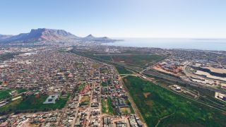 Dense urban neighborhoods surround an airfield near the coastline, with highways crossing green spaces and a flat-topped mountain rising beyond.