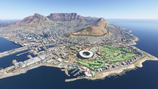 Cape Town’s coastline curves around harbors and an oval stadium, with dense urban development extending toward Table Mountain beneath clear skies.
