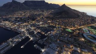 Cape Town’s illuminated waterfront shows harbor basins, docked ships, and an oval stadium beneath Table Mountain at dusk.