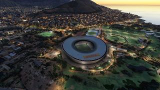 An aerial view shows an oval stadium surrounded by illuminated streets, sports fields, and coastal neighborhoods beneath a dark hillside at dusk.