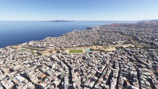 A dense coastal city surrounds a green sports field and stone fortifications, with a harbor and offshore island beyond.