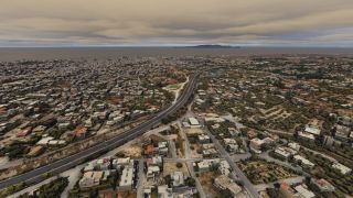 A divided highway curves through a coastal city of low-rise buildings, with an offshore island beneath layered gray clouds.