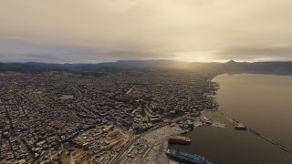 A coastal city surrounds a harbor with docked ferries, a marina, and a long breakwater beneath cloud-covered mountains and golden skies.