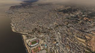 A dense coastal city stretches inland beneath hazy hills, with a waterfront stadium, harbor, airport runway, and intersecting highways.