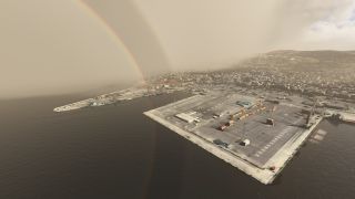A rainbow arcs above a coastal harbor with colorful shipping containers, concrete quays, docked vessels, and buildings spreading across nearby hills.