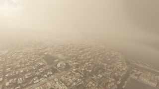 Dense beige haze obscures a coastal city, where tightly spaced low-rise buildings and gridded streets extend toward the shoreline.