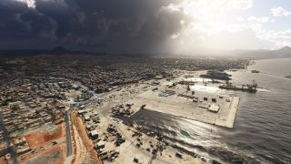 A coastal city surrounds a harbor with docked ships, cargo cranes, and broad quays beneath dark clouds and patches of sunlight.