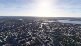 An aerial view shows dense city blocks surrounding a narrow waterway crossed by bridges, with broad lakes extending toward the horizon.