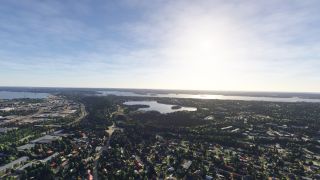 Tree-lined residential neighborhoods and industrial buildings surround several lakes, with wooded islands and sunlit water extending toward the horizon.