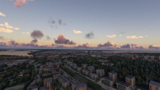 Apartment buildings and tree-lined roads extend toward a waterfront skyline beneath scattered pink and purple clouds.