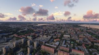 An aerial view shows dense city blocks, tree-lined streets, and distant waterways beneath scattered pink and gray clouds.