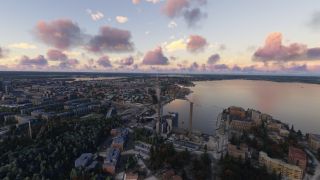 A waterfront city stretches around a broad lake, with industrial smokestacks, apartment buildings, and tree-lined streets beneath pink clouds.