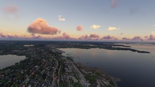 A shoreline town borders broad waterways, with roads threading through wooded neighborhoods beneath scattered pink and orange clouds.