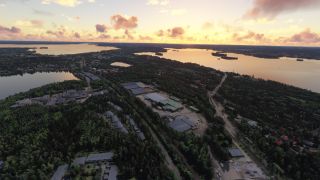 Forested neighborhoods, industrial buildings, and roads border interconnected lakes beneath a golden sky with scattered pink clouds.