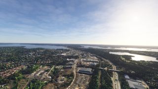 Industrial buildings and residential neighborhoods extend between wooded lakeshores, with a divided highway and overpass visible in the foreground.