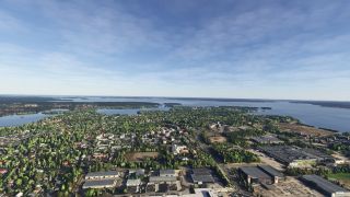An aerial view overlooks tree-lined neighborhoods and large commercial buildings beside broad waterways dotted with wooded islands.