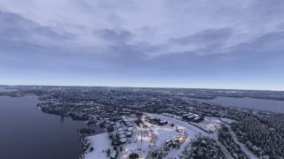 A snow-covered city stretches between lakes, with illuminated winding roads, industrial buildings, and a tall observation tower beneath overcast skies.