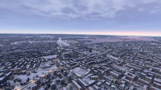 Snow-covered buildings and illuminated roads spread across a waterfront city beneath layered clouds and a pink horizon.