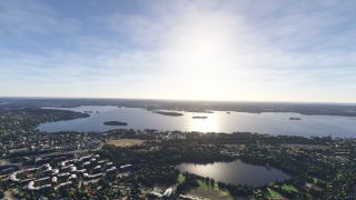Sunlight reflects across a broad lake dotted with wooded islands, while neighborhoods and a smaller tree-lined lake fill the foreground.