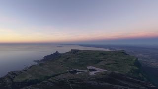 A flat-topped coastal mountain contains two reservoirs, with ocean to the left and urban development beneath a pink-tinged sky.