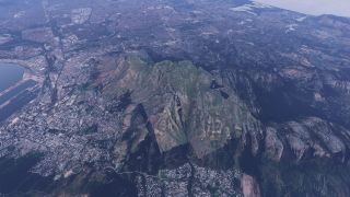 A rocky mountain massif rises above dense coastal neighborhoods, with harbor docks to the left and reservoirs among the ridges.