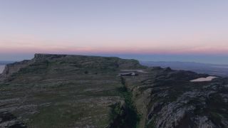 A rocky mountain plateau features steep cliffs, a deep vegetated ravine, and small lakes beneath a pink and blue sky.