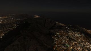 A flat-topped mountain rises between illuminated city streets and a dark coastline beneath the night sky.