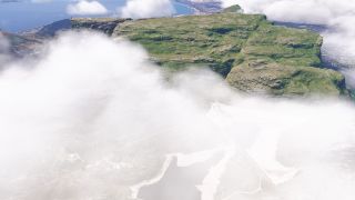 Low clouds partially obscure a rocky, flat-topped mountain, with reservoirs below and a coastal city beside blue water in the distance.