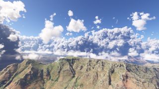 A flat-topped mountain ridge with steep rocky cliffs and green slopes stretches beneath towering clouds, with urban terrain visible beyond.