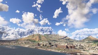 Cape Town’s waterfront buildings line the shore beneath Table Mountain, with scattered cumulus clouds filling the blue sky.