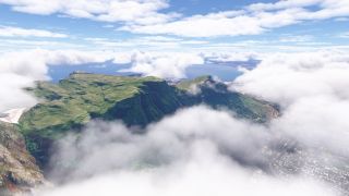 Low clouds partially obscure a flat-topped mountain with steep green cliffs, while coastal buildings and blue water extend beyond.
