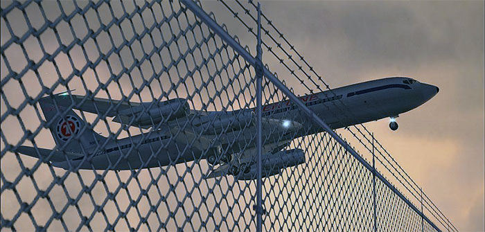Aircraft flying over airport perimeter fence.